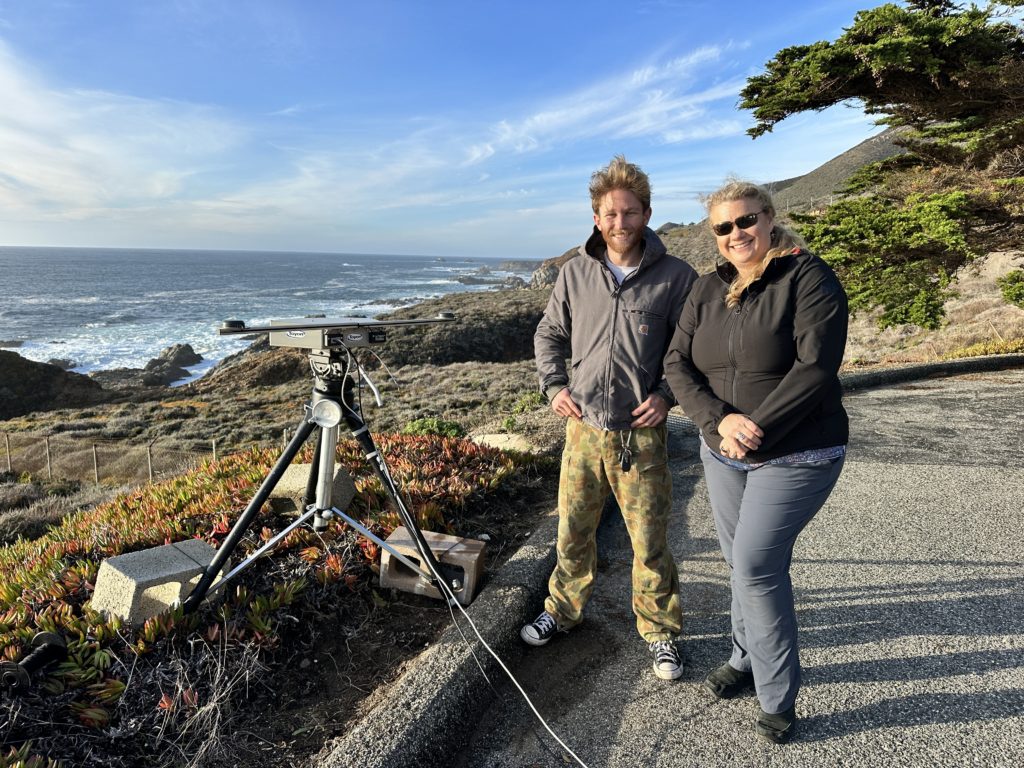Two Marine Observer team members stand next to the camera on the coast of Carmel with the ocean in the background. 